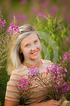 Cute smiling blonde woman with wildflowers. Summer portrait of a woman with rose-tea in the field