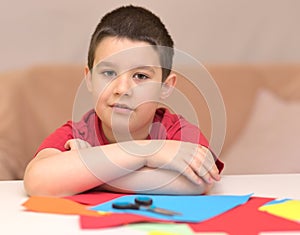 Cute smiling boy is cutting paper using scissors