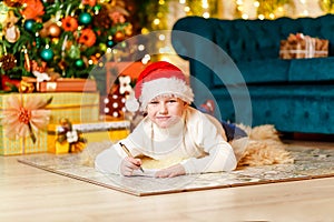 Cute smiling boy in Santa`s red cap writes a letter to Santa Claus for Christmas