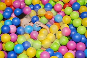 Cute smiling boy in sponge ball pool looking at camera. Child playing with colorful balls in playground ball pool