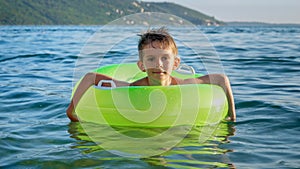 Cute smiling boy swimming in the inflatable ring on calm sea waves. Family holidays, vacations, summertime.
