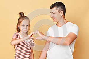 Cute smiling brwon haired little girl standing with her father and making heart shape with hands together expressing love family