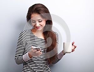 Cute smiling casual woman texting sms on mobile phone and drinking coffee