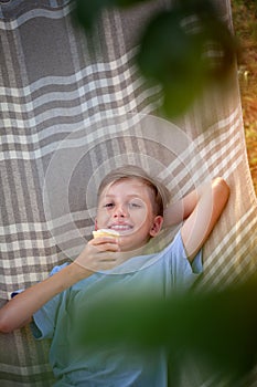 Cute smiling caucasian boy eating ice cream and having fun on hammock in backyard or outdoor.Child staying cool in the summer heat