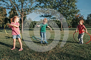 Cute smiling Caucasian preschool girl boys friends playing with hoola hoop in park outside. Kids sport activity. Lifestyle happy