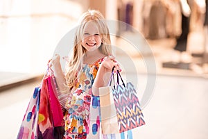 Cute smiling child girl 4-5 year old hold paper bags shopping in store mall making purchases. Buy clothes with season sales.