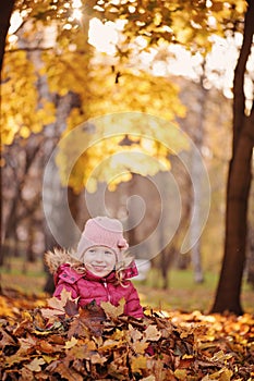 Cute smiling child girl having fun on the autumn walk and sitting in leaves