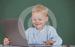 Cute smiling child using laptop computer, kid boy studying through online e-learning. Little funny programmer.