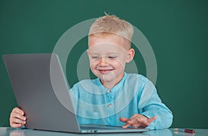 Cute smiling child using laptop computer, kid boy studying through online e-learning. Little funny programmer.