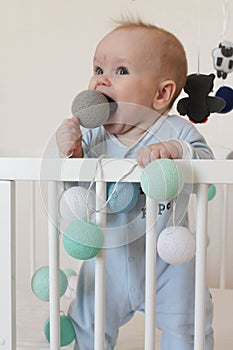 Cute smiling european baby stands in a white canopy bed and plays with balls.