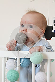 Cute smiling european baby stands in a white canopy bed and plays with balls.