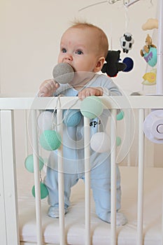 Cute smiling european baby stands in a white canopy bed and plays with balls.