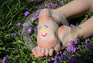Cute smiling face is drawn on the children`s bare feet lying among the flowers