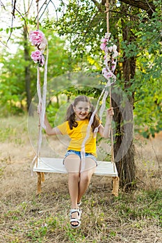 Cute smiling girl having fun on a swing in tree forest