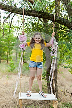 Cute smiling girl having fun on a swing in tree forest