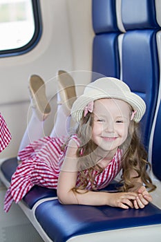Cute smiling girl with long wavy hair in panama hat lying on armchair in the train