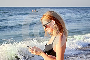 Cute smiling girl texting with her mobile phone message on a beach. Nice relax