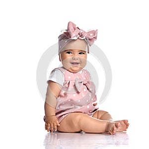 Cute smiling infant baby girl toddler in polka-dot dress and headband with bow sits on the white floor