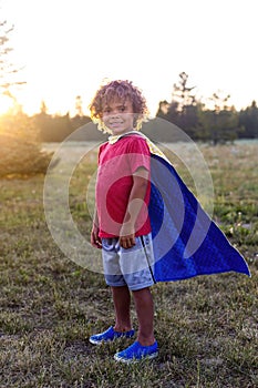 Cute smiling little African American boy wearing a cape outdoors and pretending to be a super hero