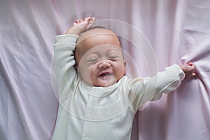Cute smiling little Asian 2 - 3  months old newborn baby girl child lying in bed wakes up and stretches, Newborn daughter relaxing