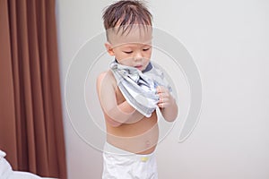 Cute smiling little Asian 2 years old toddler boy child in bed concentrate on putting on his striped T Shirt