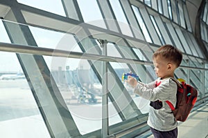 Cute smiling little Asian 2 years old toddler boy child having fun playing with airplane toy while wait for his flight at airport