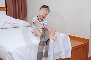 Cute smiling little Asian 2 years old toddler boy child sitting in bed concentrate on putting on his pants