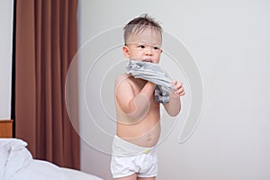 Cute smiling little Asian 2 years old toddler boy child in bed concentrate on putting on his striped T Shirt photo