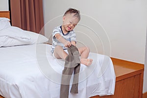 Cute smiling little Asian 2 years old toddler boy child sitting in bed concentrate on putting on his pants photo