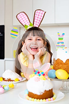 A cute smiling little girl with bunny ears prepares an Easter cake and painted eggs. Religious holiday