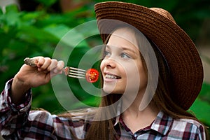 Cute smiling little girl with cherry tomato on green background