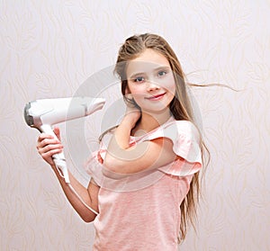 Cute smiling little girl child drying her long hair with hair dryer