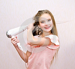 Cute smiling little girl child drying her long hair with hair dryer