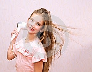 Cute smiling little girl child drying her long hair with hair dryer