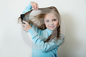 Cute smiling little girl combing her hair comb makes hair