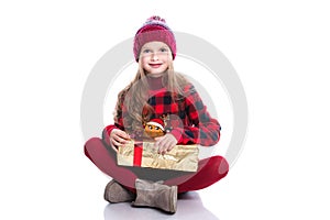 Cute smiling little girl with curly hairstyle wearing knitted sweater, scarf and hat holding christmas gift isolated on white