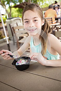 Cute smiling little girl eating a delicious bowl of ice cream at an outdoor cafe