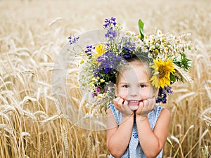 Cute smiling little girl with flower wreath on the meadow at the farm. Portrait of adorable small kid outdoors.