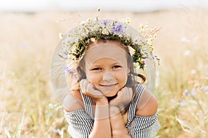 Cute smiling little girl with flower wreath on the meadow. Portrait of adorable small kid outdoors