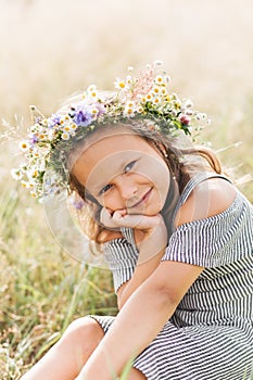 Cute smiling little girl with flower wreath on the meadow. Portrait of adorable small kid outdoors