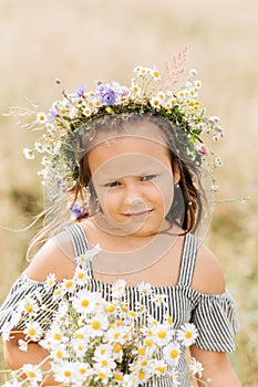 Cute smiling little girl with flower wreath on the meadow. Portrait of adorable small kid outdoors