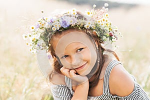 Cute smiling little girl with flower wreath on the meadow. Portrait of adorable small kid outdoors