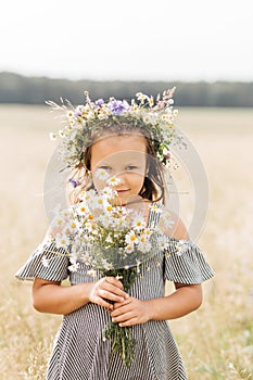 Cute smiling little girl with flower wreath on the meadow. Portrait of adorable small kid outdoors