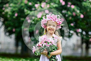 Cute smiling little girl with flower wreath on the park. Portrait of adorable small kid outdoors. Midsummer. Earth Day