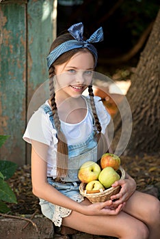 Cute smiling little girl holds basket  with apples at the farm