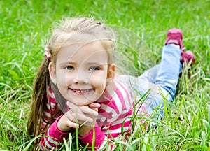 Cute smiling little girl lying in grass on the meadow