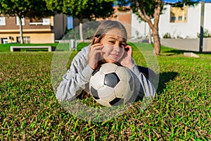 Cute smiling little girl lying on the grass in a nice park with her used soccer ball