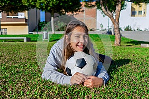 Cute smiling little girl lying on the grass in a nice park with her used soccer ball