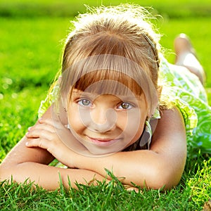 Cute smiling little girl lying on a green grass in the park on a