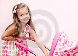 Cute smiling little girl playing with her toy carriage